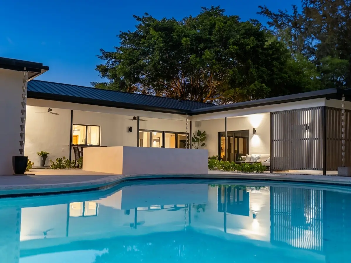 Pool lit at night, house glowing behind slat wall screen
